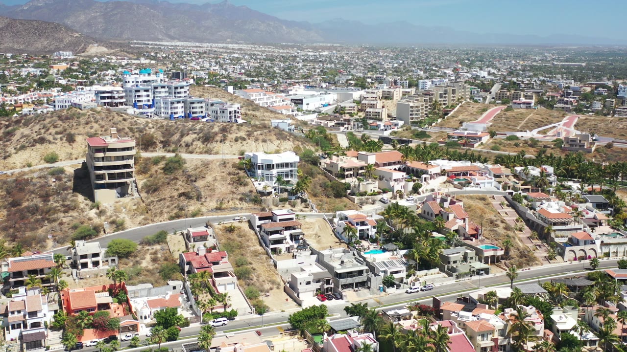Aerial view over dry hillside homes, roads, and distant mountains.