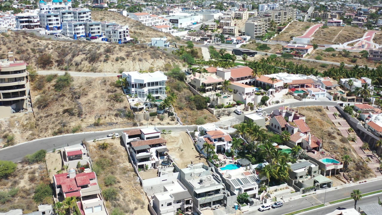 Drone-style view across hillside houses and distant buildings.