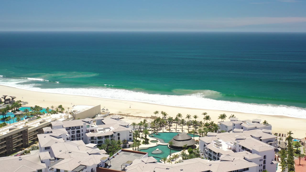 Aerial view of beachfront resort pools, palms, sand, and turquoise ocean.