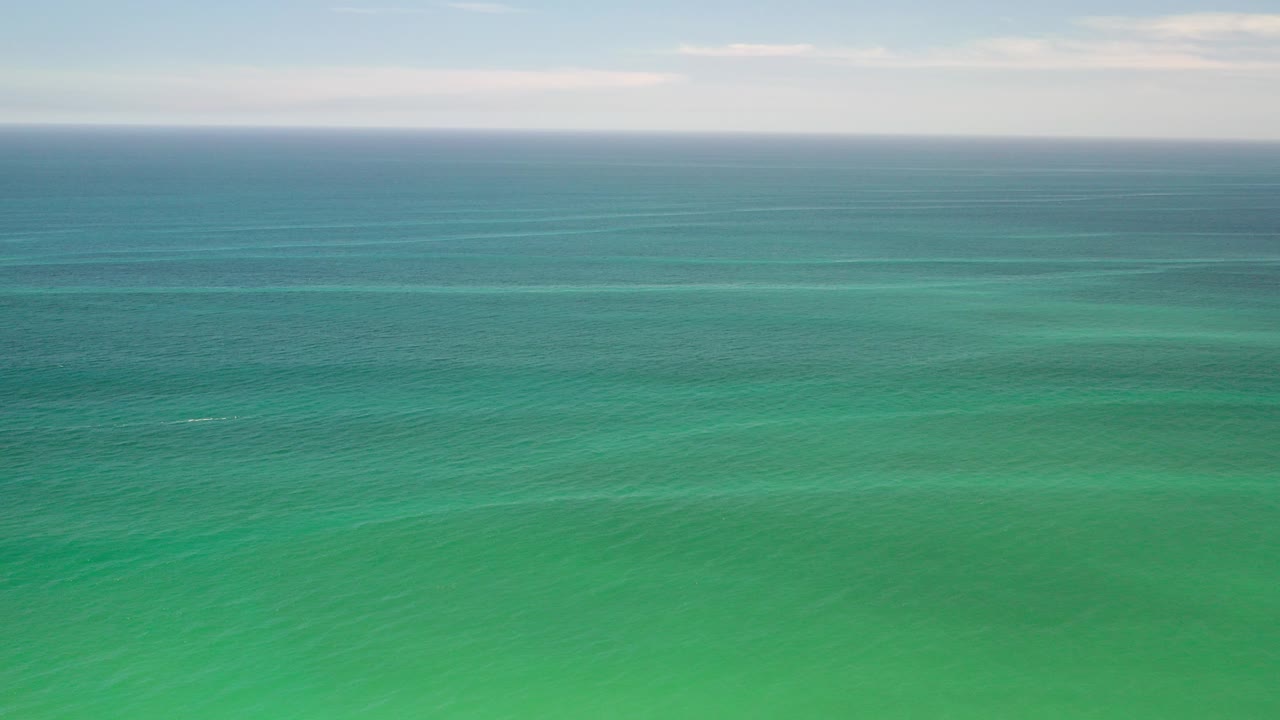 Wide aerial view of teal ocean and pale sky horizon.
