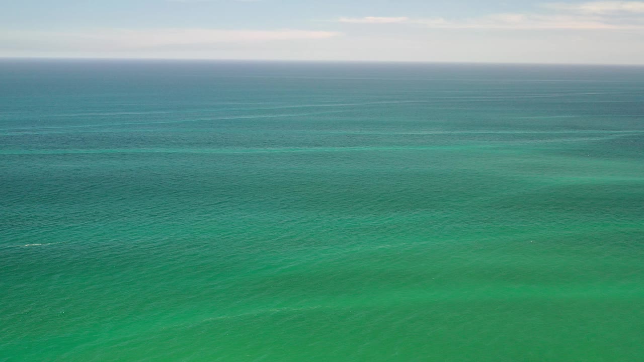 Wide green ocean in Los Cabos, Mexico beneath a pale sky, with a level horizon and no visible people.