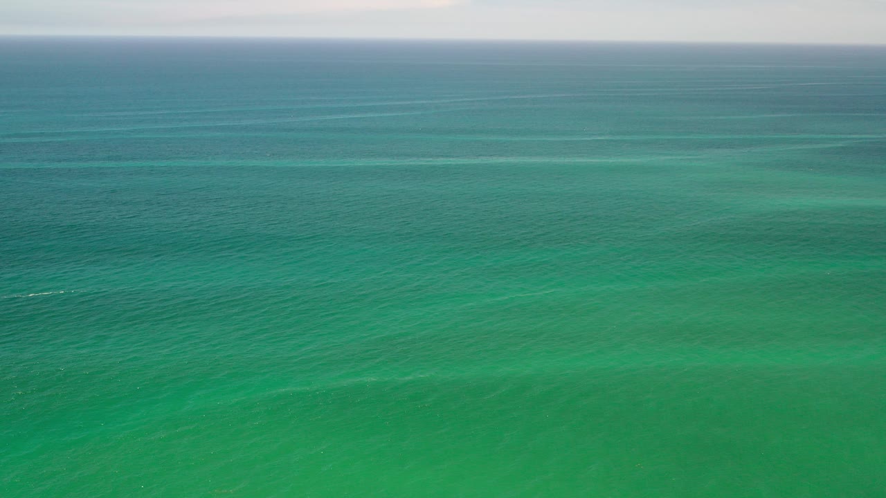 Wide aerial view of green ocean water in Los Cabos, Mexico, with faint swell lines near the horizon and no visible people.