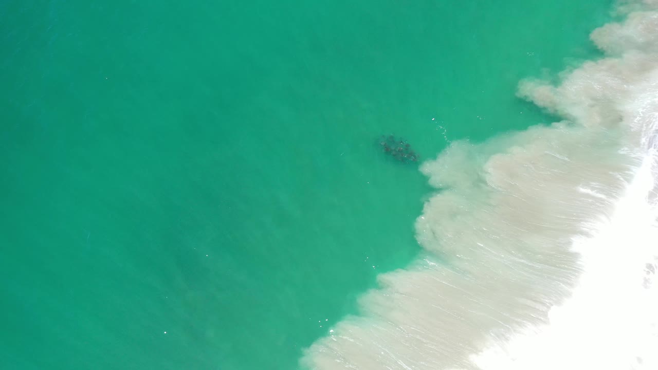 Overhead Los Cabos shoreline frame with turquoise water on the left, white surf over pale sand on the right, and no visible people.