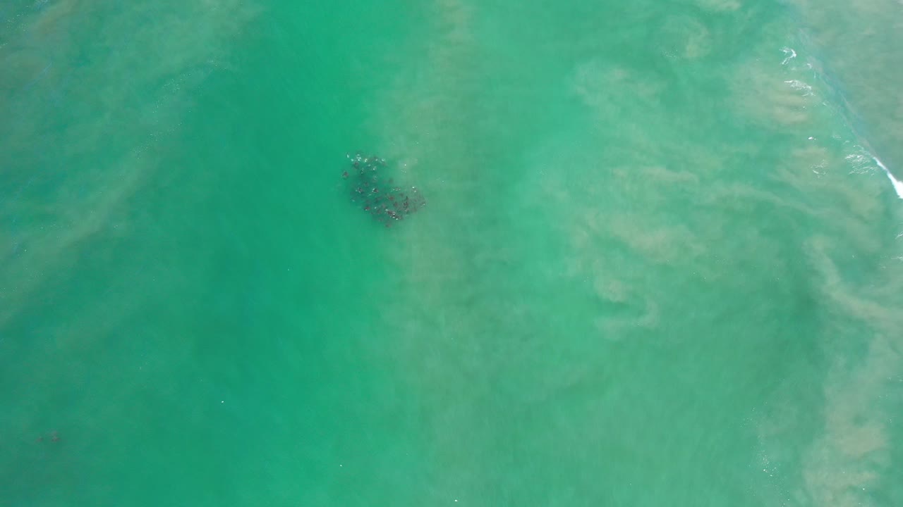 Overhead aerial view of turquoise water in Los Cabos, Mexico, with pale underwater sand patterns, a dark submerged patch left of center, and no visible people.