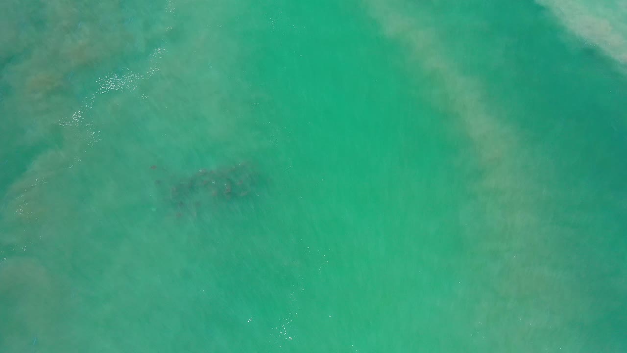 Overhead Los Cabos water view with green-blue color, soft pale streaks, and a darker submerged patch near the center, no visible people.