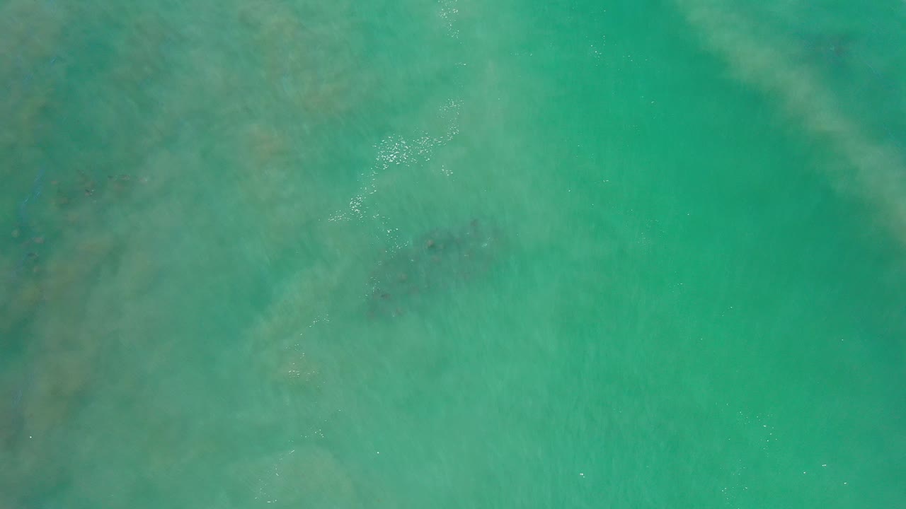 Top-down turquoise ocean water with darker underwater patches.