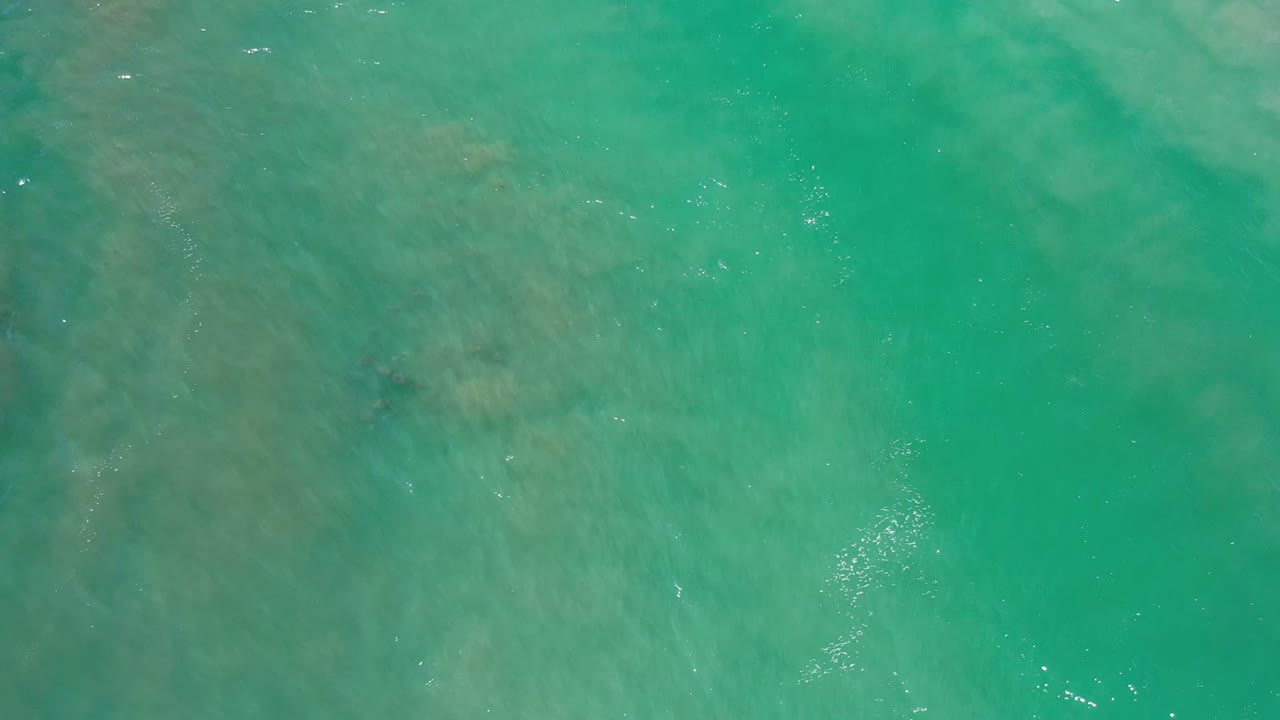 Overhead view of blue-green water in Los Cabos, Mexico, with faint darker patches below the surface and no visible people.