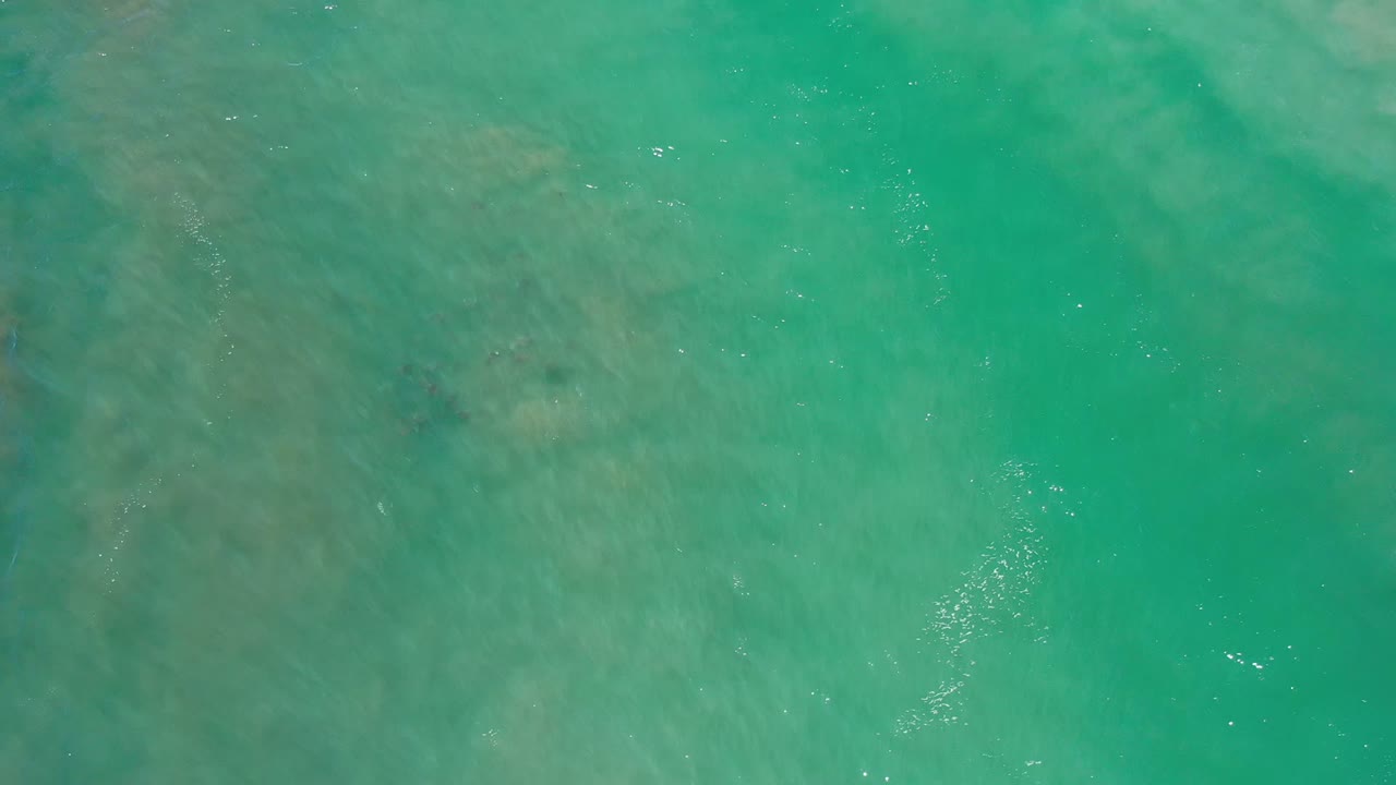 Turquoise Los Cabos water fills the frame from above, with small bright reflections and no visible people.