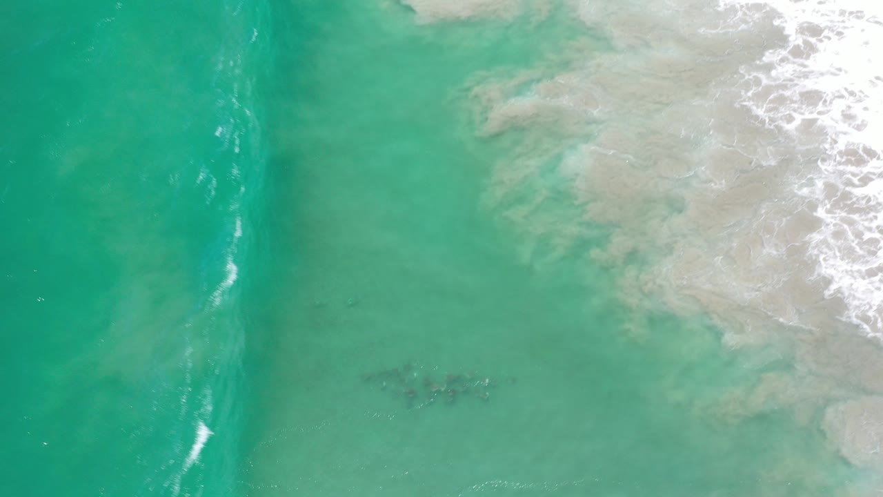 Overhead green ocean water beside pale surf and sand.