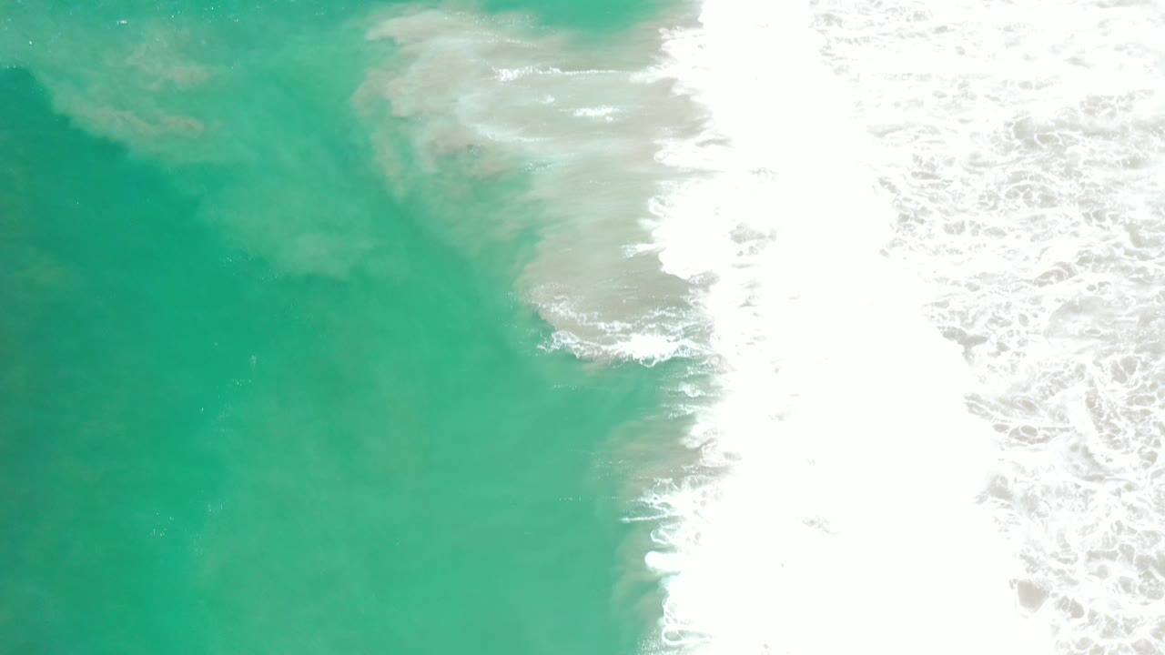 Aerial-looking frame of green sea water and dense white foam pushed farther across the right side in Los Cabos, Mexico, with no visible people.