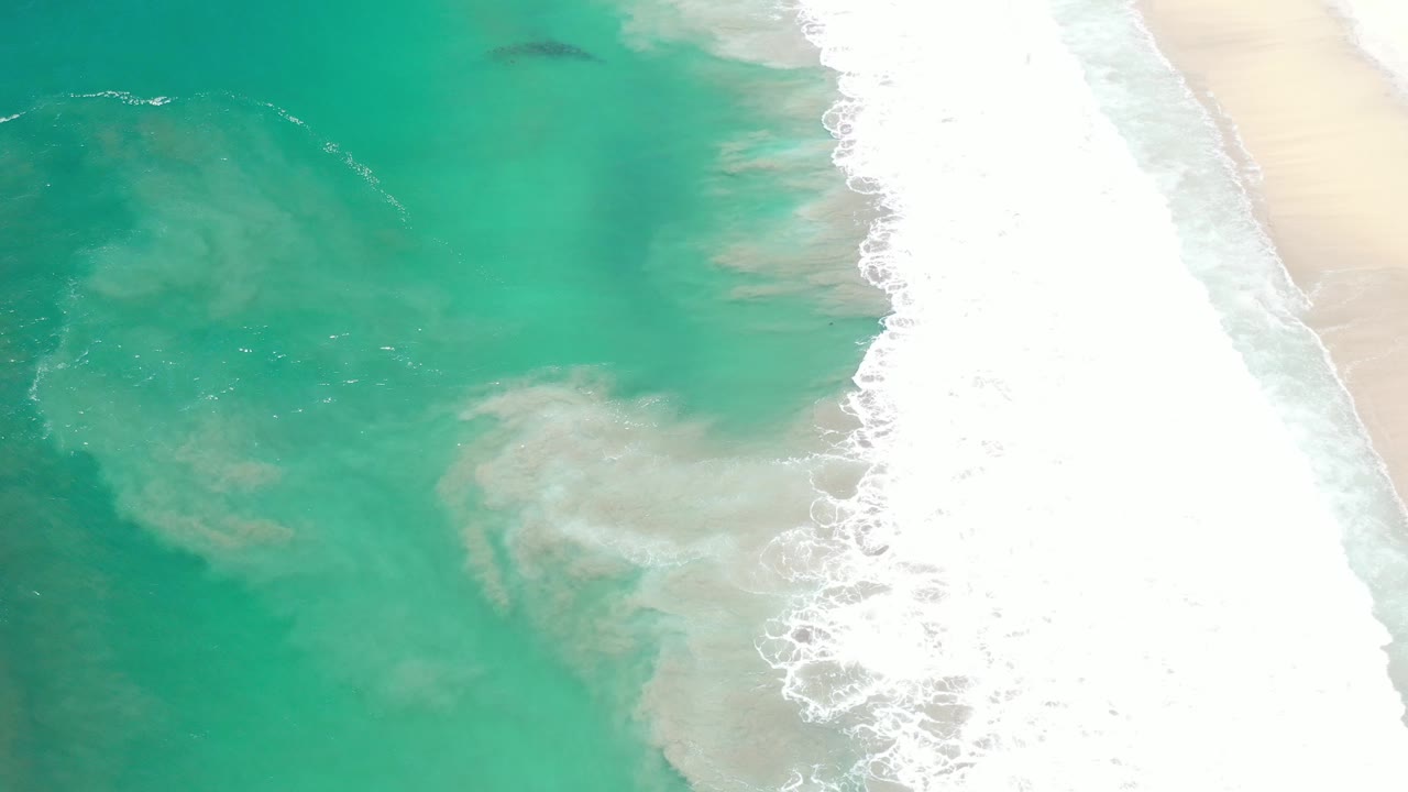 Turquoise sea with breaking waves along sandy shore