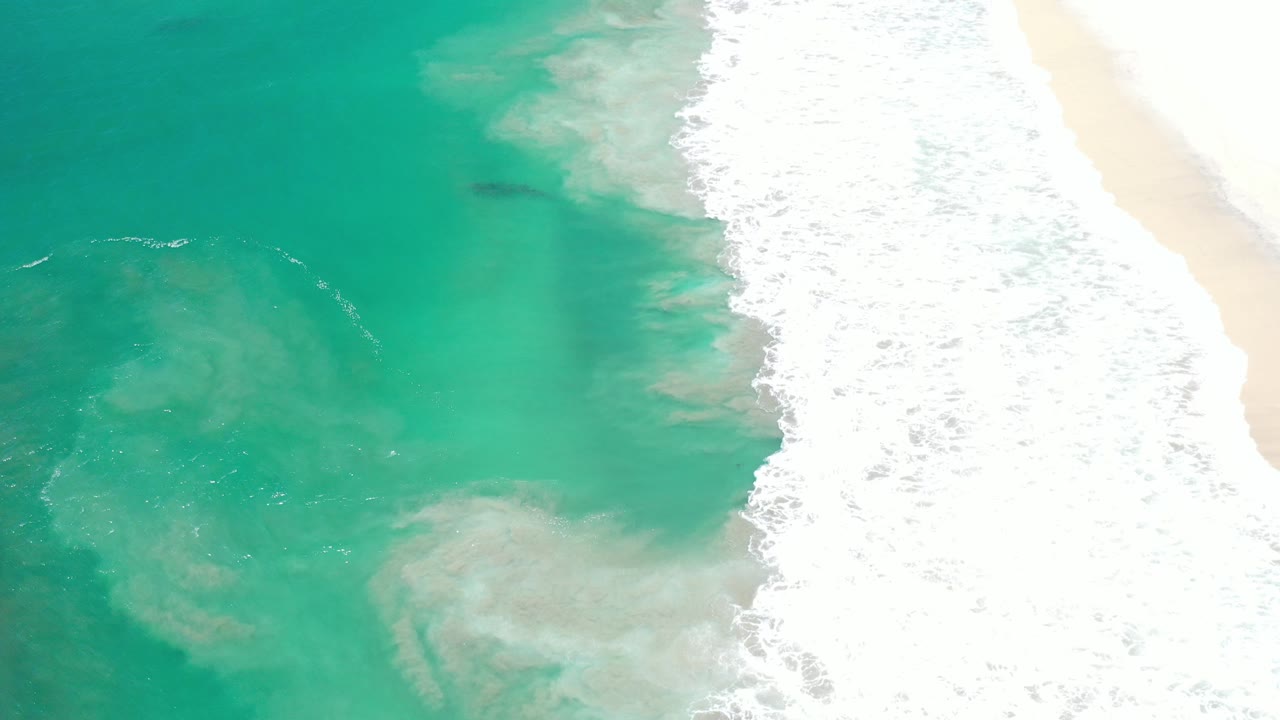 Overhead turquoise water and white surf beside pale sand.