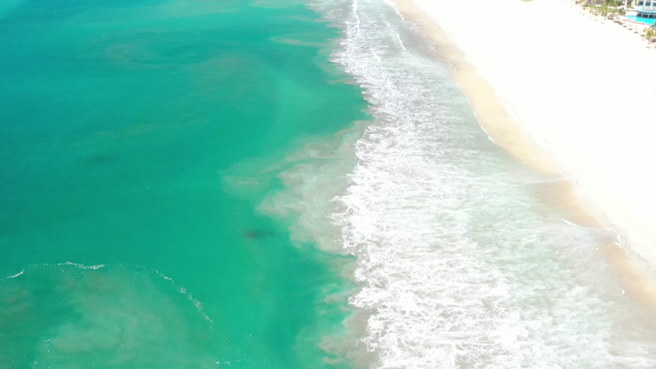 High coastal view with surf, sand, and a small glimpse of buildings.