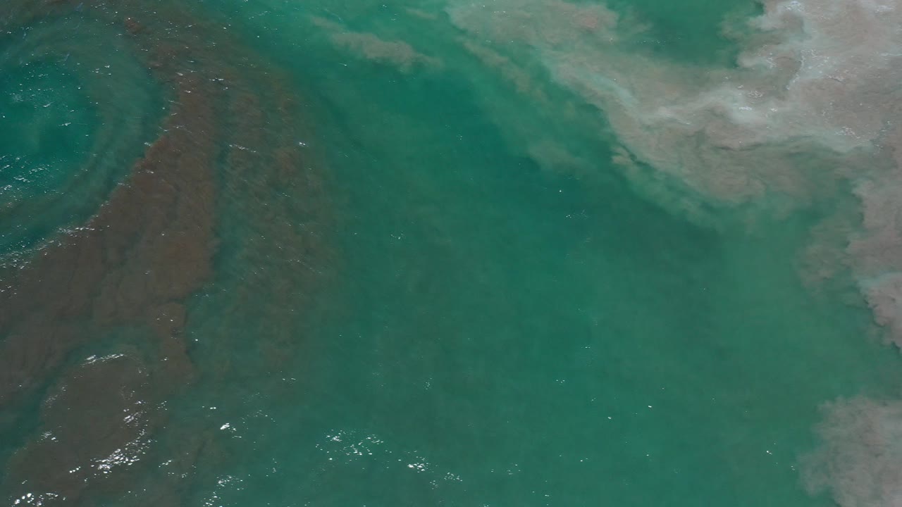 Teal ocean water with brown swirl and white foam.