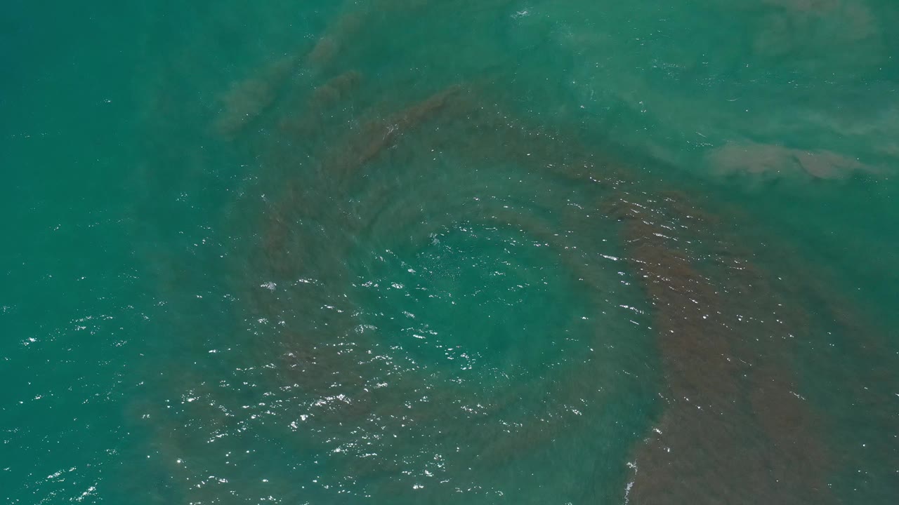 Shallow turquoise water with a central algae swirl and light reflections