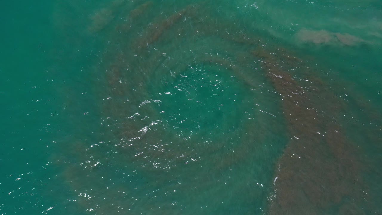 Turquoise ocean water with brown sand swirling below the surface