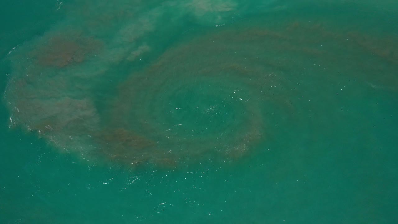 Aqua ocean water with a dark circular swirl beneath the surface.