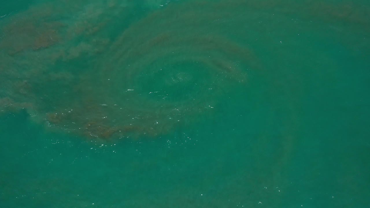 Top-down aerial frame over teal ocean water in Los Cabos, Mexico, with darker submerged patches and small white ripples, no visible people.