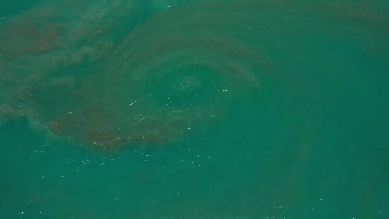Teal ocean surface with faint underwater swirls and small white ripples.