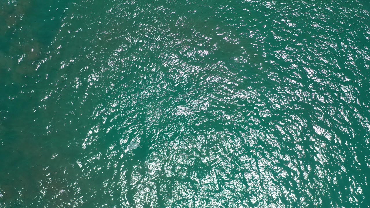 Top-down turquoise ocean water with bright sun reflections.