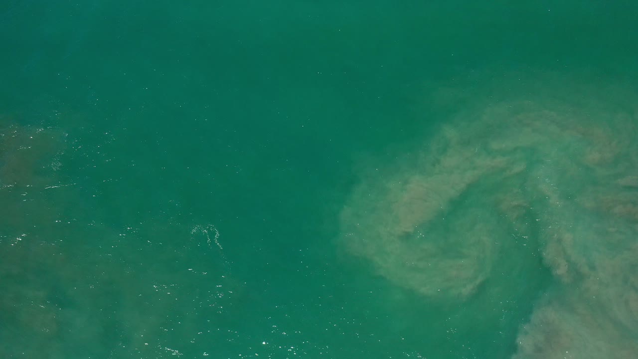 Overhead green ocean water with a submerged rock shape.
