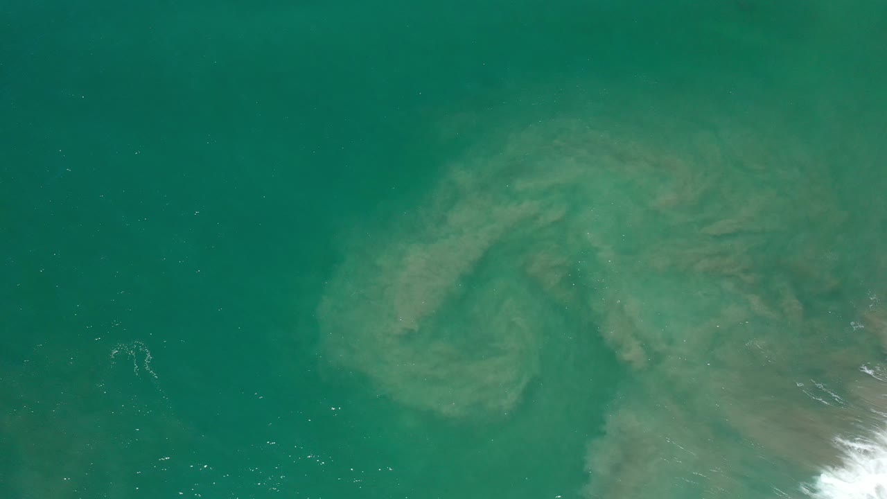 Overhead green ocean water with pale submerged sand patterns.