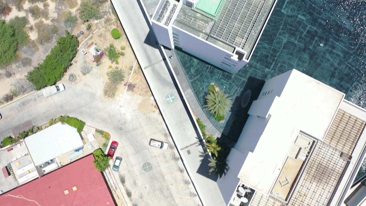 Overhead view of white buildings, road, dry land, and dark turquoise water.
