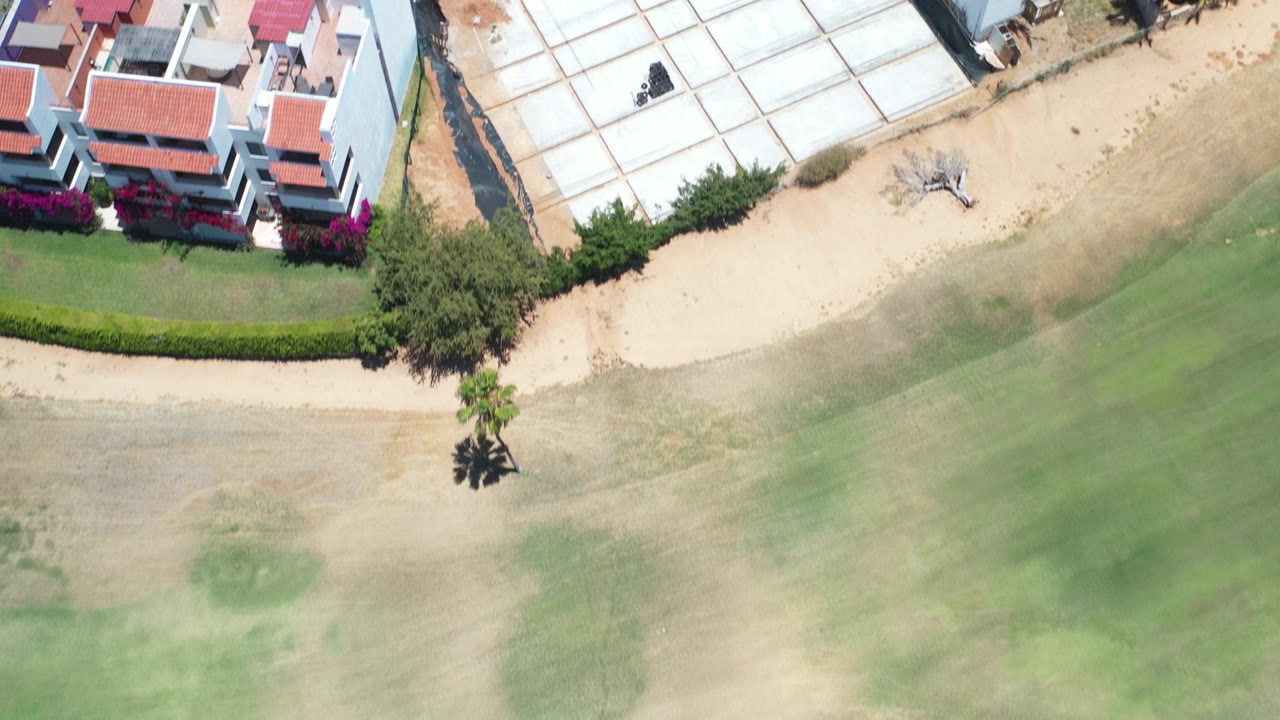 Top-down aerial view of red-roofed buildings beside sand and green landscaping.