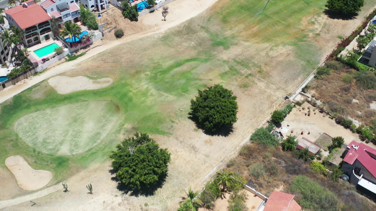 Aerial view of a dry golf course with sand bunkers, trees, homes, and pools.
