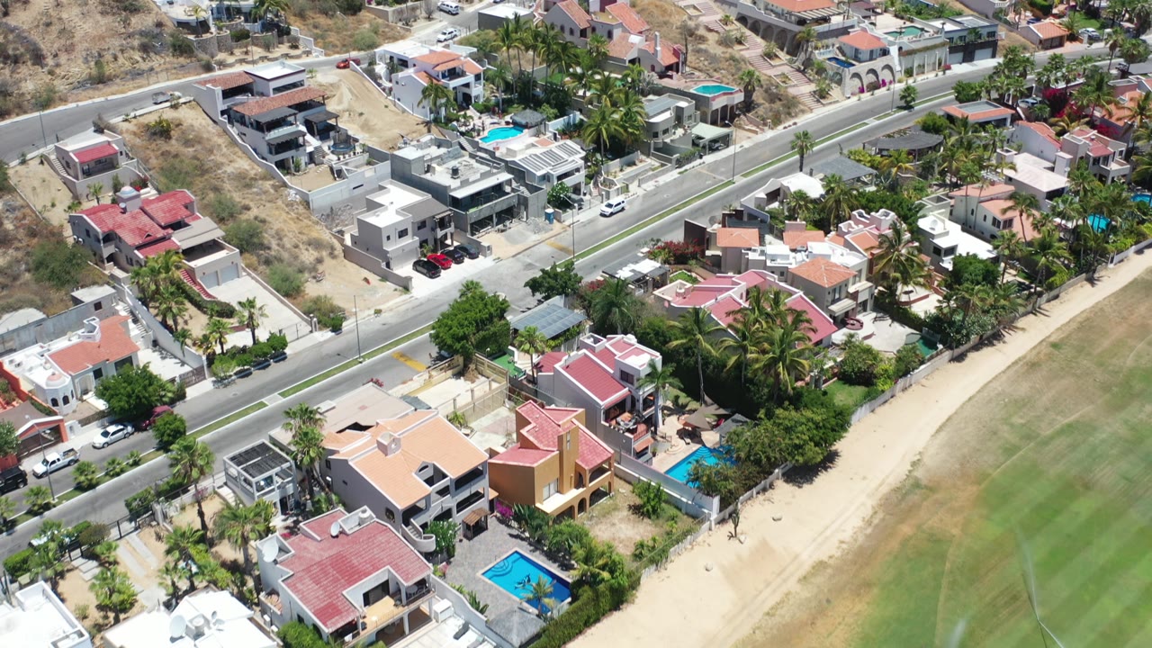 Aerial view of homes and a roadway beside a dry hill and green grounds.