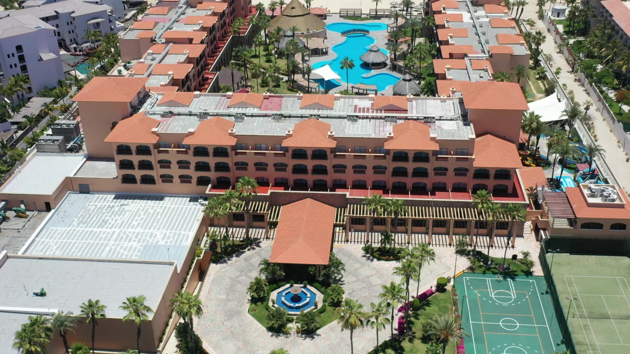 Aerial view of a resort complex with terracotta roofs, pool, courtyard, and basketball court.