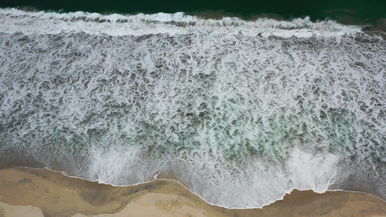 Overhead surf breaking onto a sandy beach.
