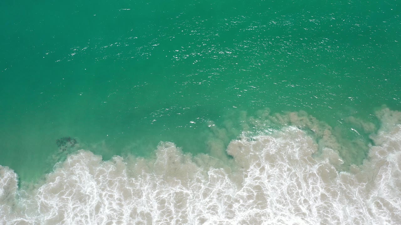 Overhead turquoise ocean waves breaking onto pale sand.