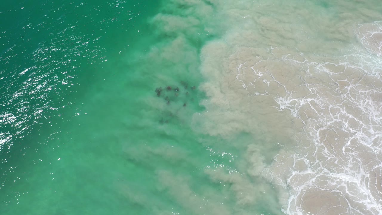 Overhead turquoise water meeting pale sandy surf