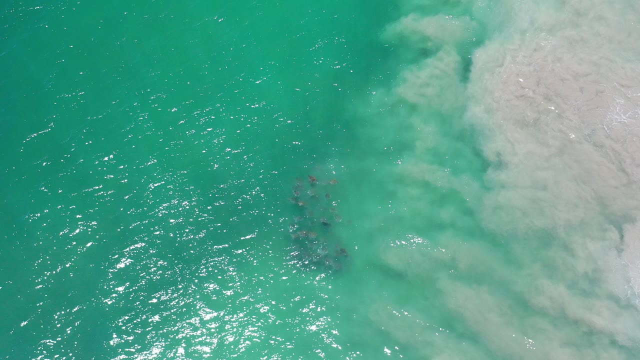 Turquoise ocean water with foam and submerged dark rocks.