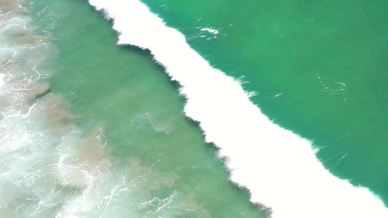 Overhead green coastal water with white surf and submerged rocks.
