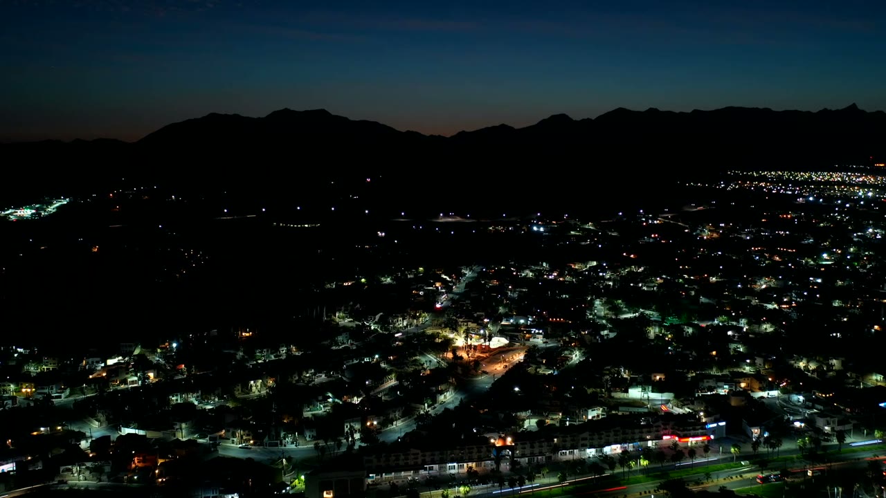 Night aerial view of city lights below a dark mountain ridge.