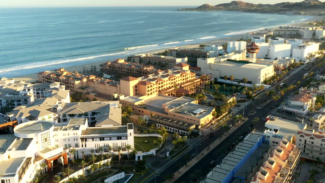 Aerial view of beach, surf, resort buildings, streets, and mountains.