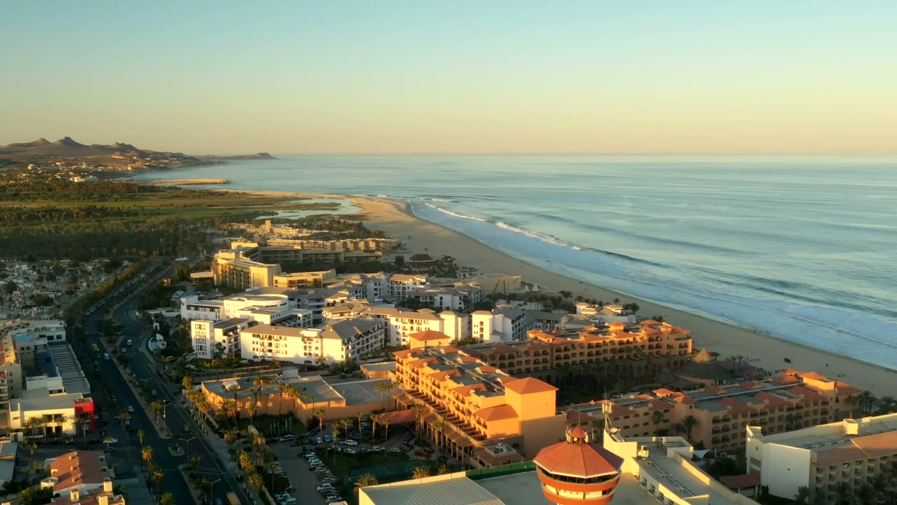 Aerial view of beachfront buildings, road, beach, and ocean at golden light.