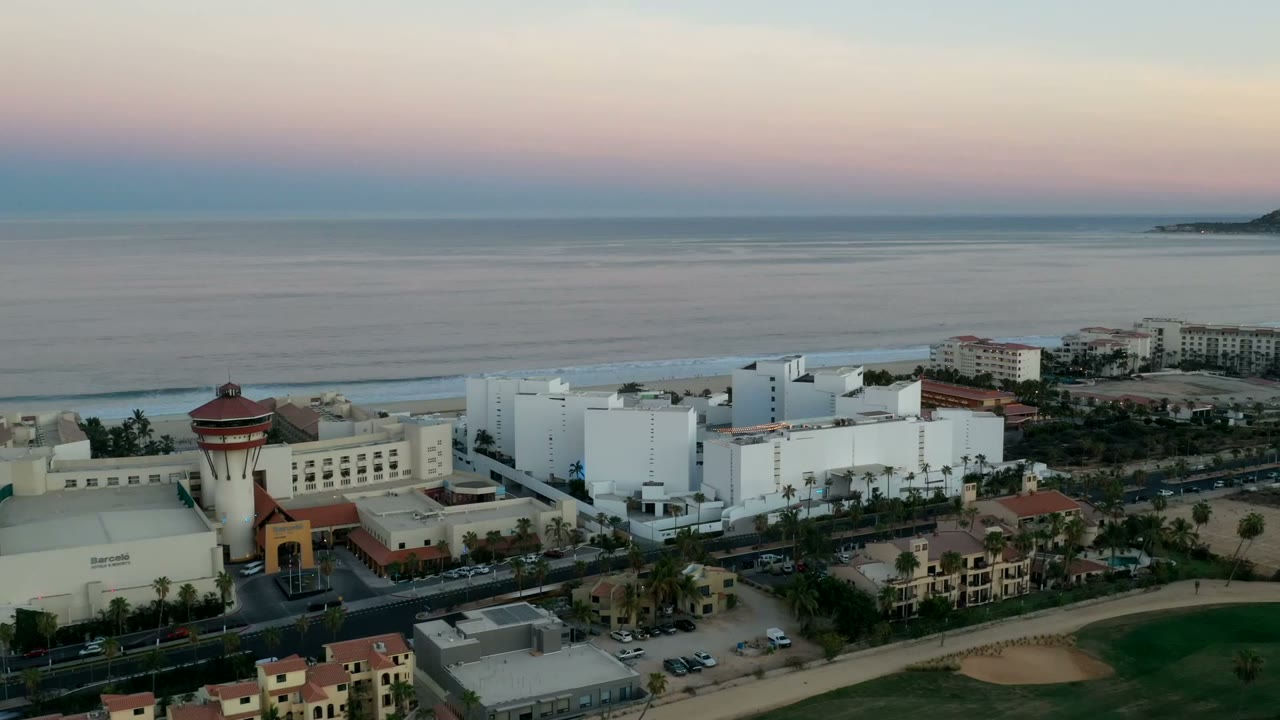 Aerial view of coastal buildings, beach, ocean, and sunset sky.