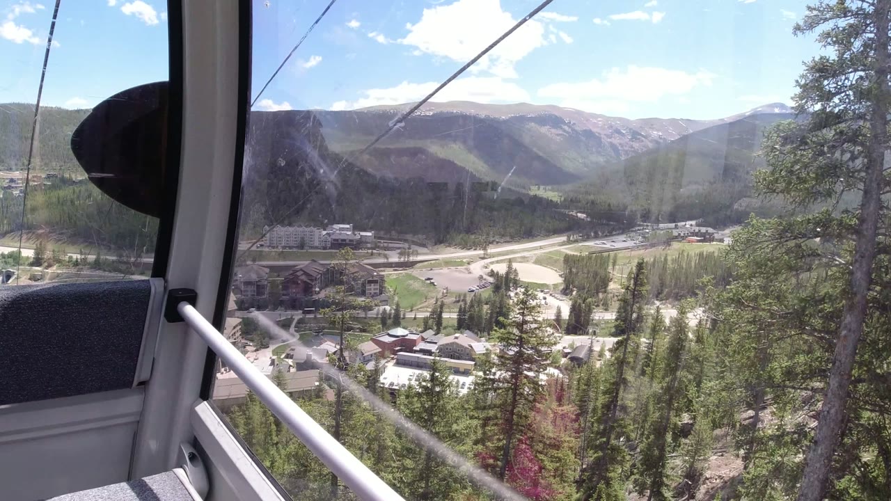 Cable car window view over trees, roads, buildings, and mountains.