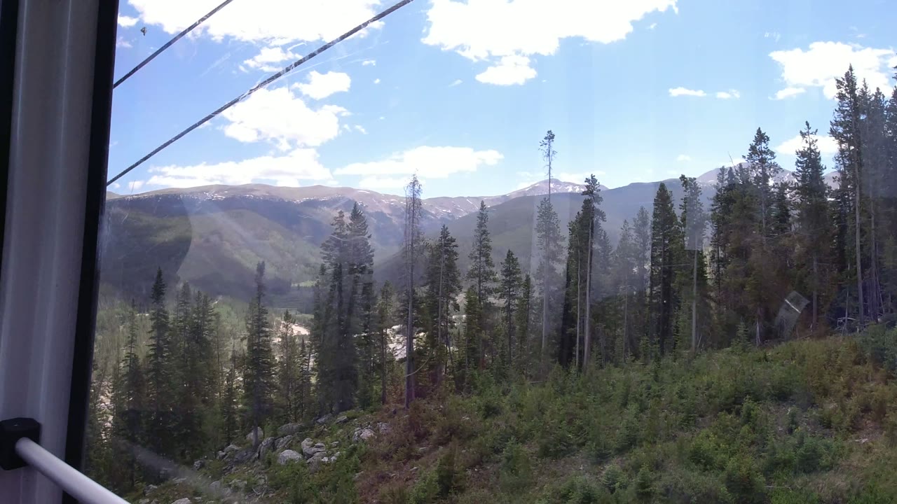 Child in a magenta jacket looking out a gondola window at forested mountains.