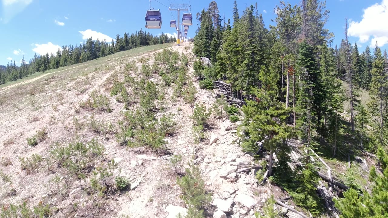 In Winter Park, Colorado, gondola cabins ride near the top of frame above a pale rocky hillside with conifers and no visible people.