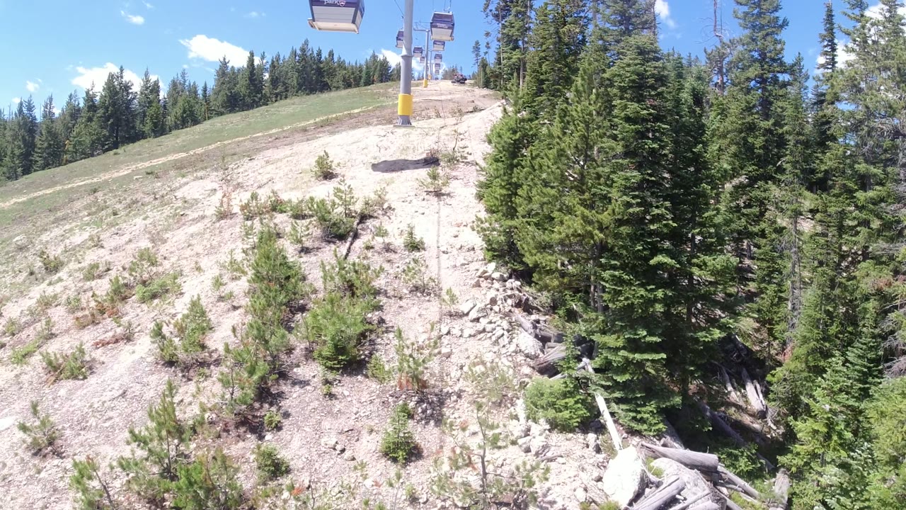 Winter Park, Colorado lift chairs hang above a light dirt slope, with a yellow tower base near the center and no visible people.