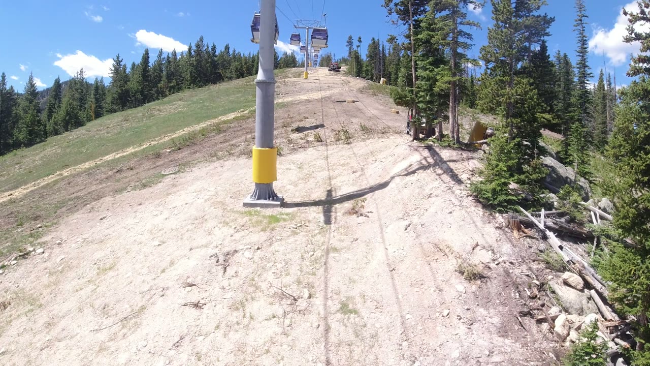Chairlift tower and cable rising over a dry mountain slope with pine forest.