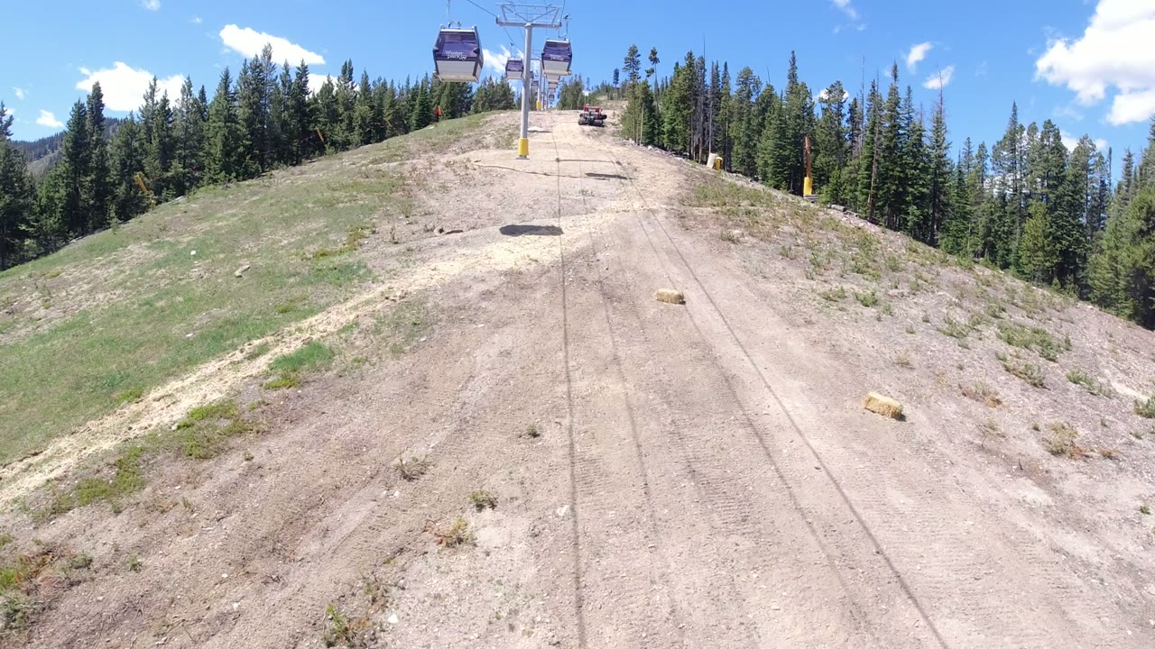 Gondola cabins above a dry mountain slope lined with pine trees.