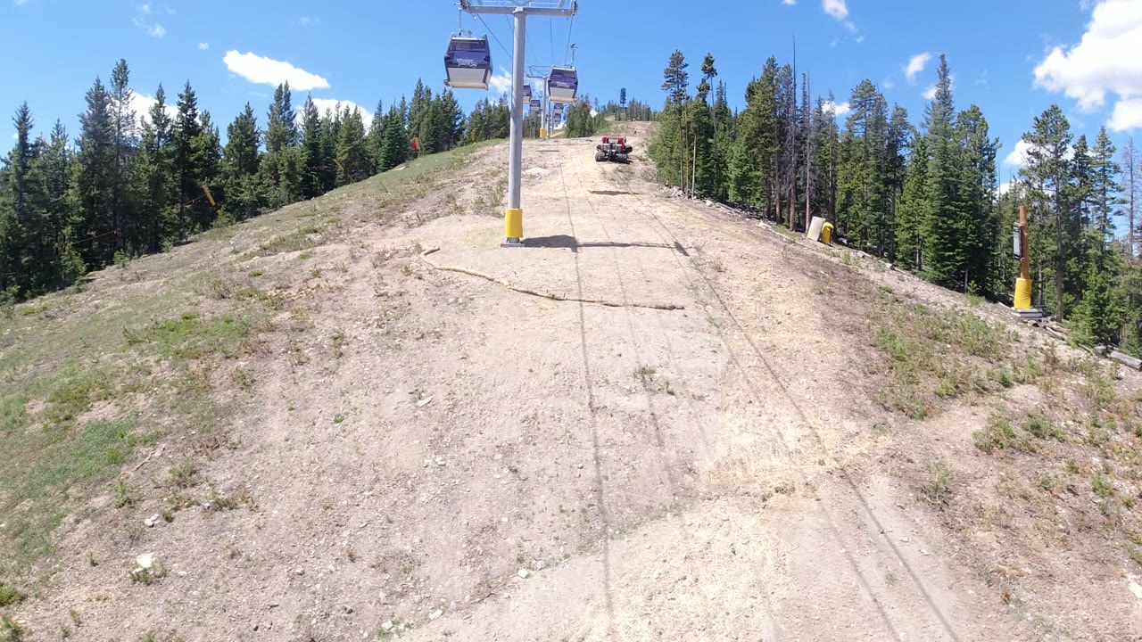 Gondola cabins over a dry mountain slope bordered by evergreen trees.