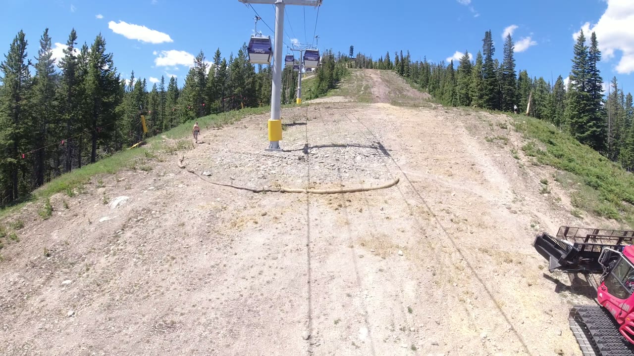Gondola cabins over a rocky hill and evergreen forest.