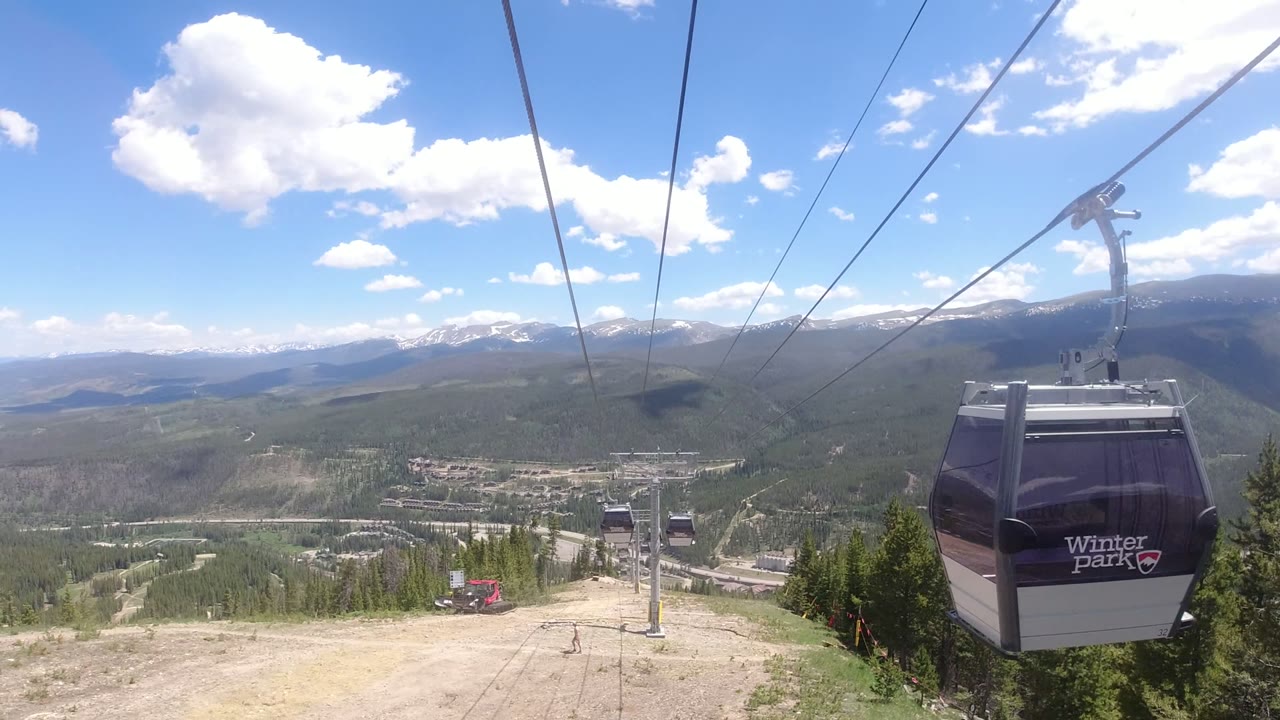 Gondola cabin on cables above a mountain valley and evergreen slope.