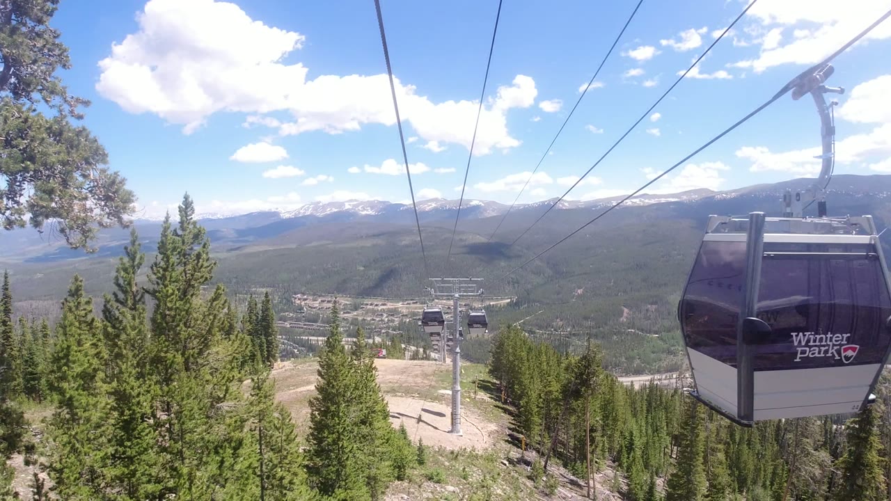 Close black gondola cabin passing over evergreen forest and mountains.